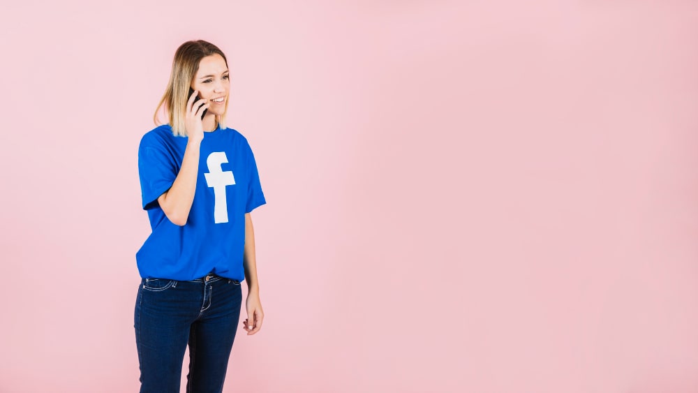 Femme souriante au téléphone portant un t-shirt facebook.