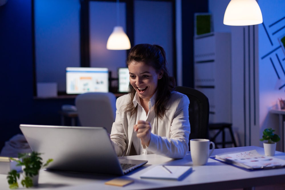Femme heureuse travaillant sur ordinateur, bureau moderne.