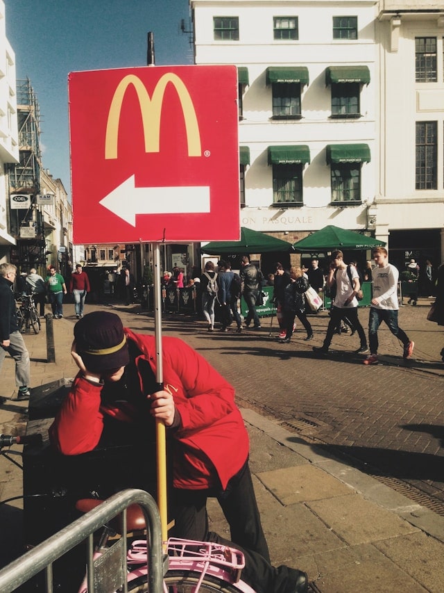 Personne dans la rue tenant un panneau McDonald's avec flèche à gauche, ville animée.